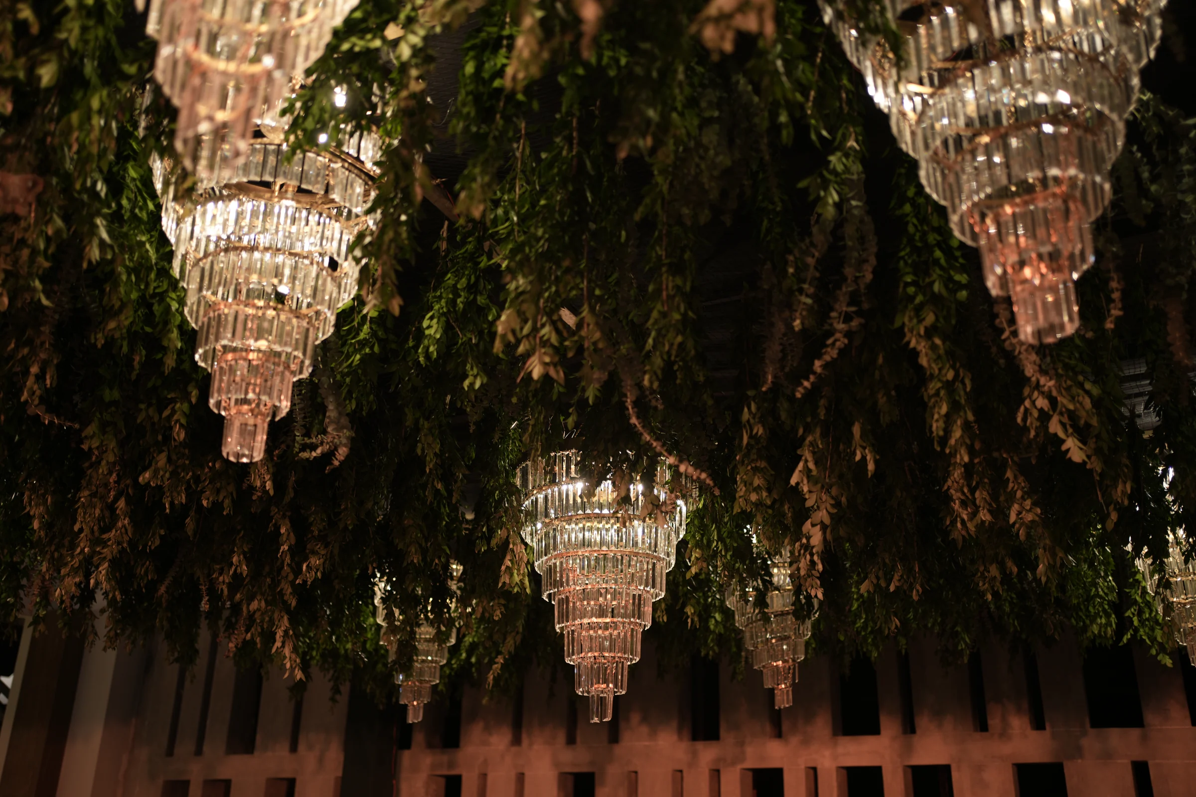 Crystal chandeliers suspended among greenery for an evening celebration