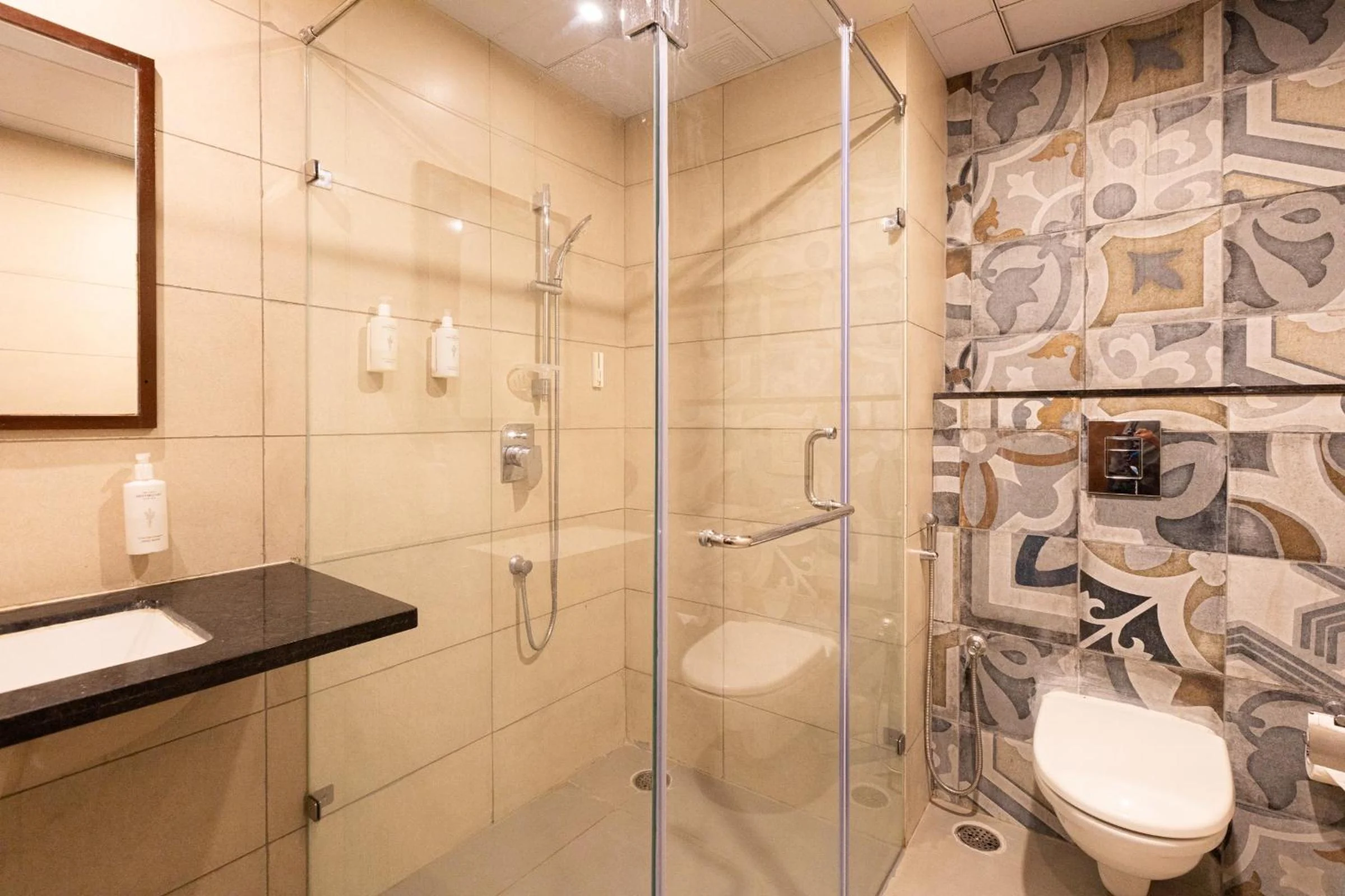 A guest bathroom with a glass shower enclosure and patterned tile wall