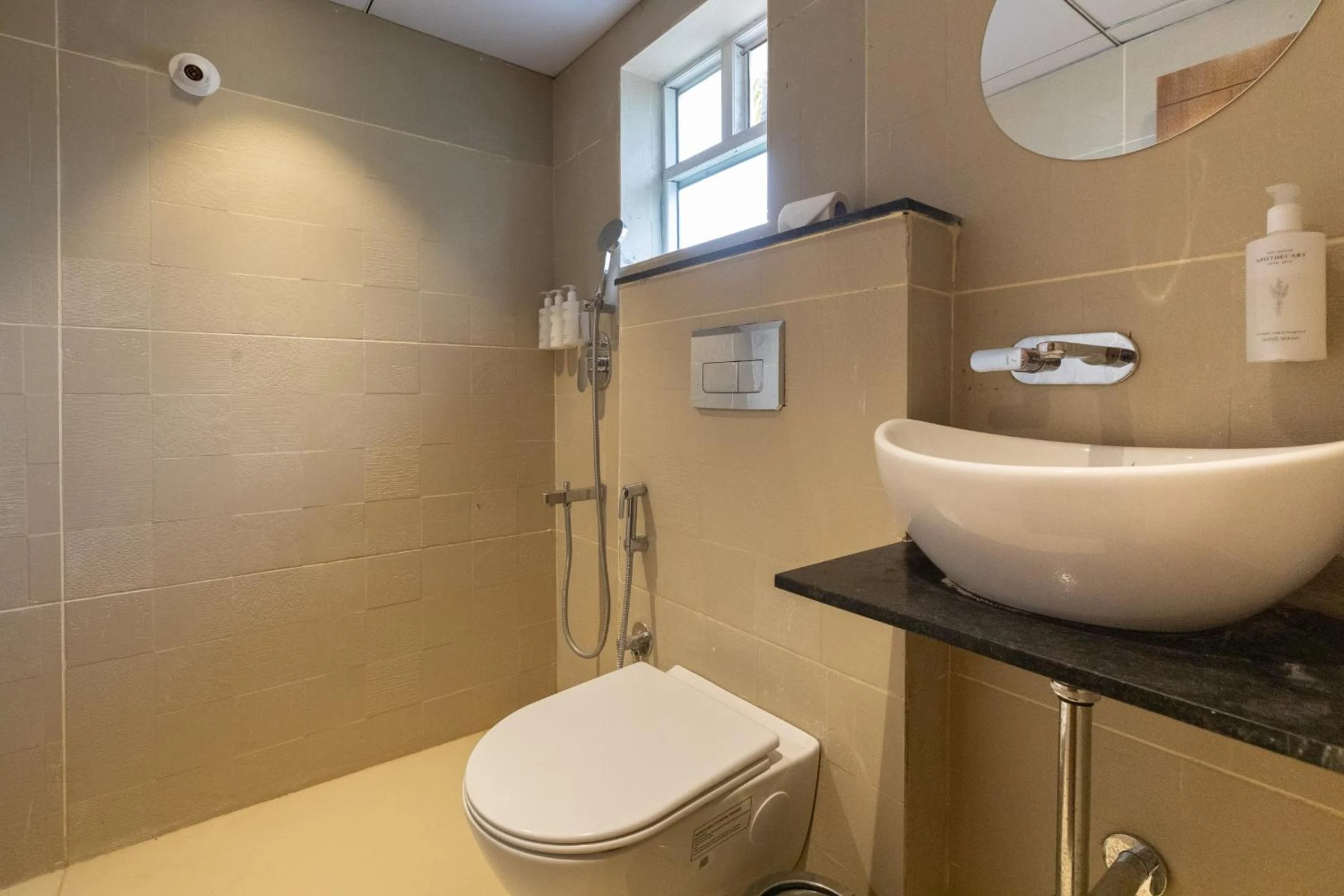 A tiled guest bathroom with a round basin, wall-mounted toilet and shower fittings