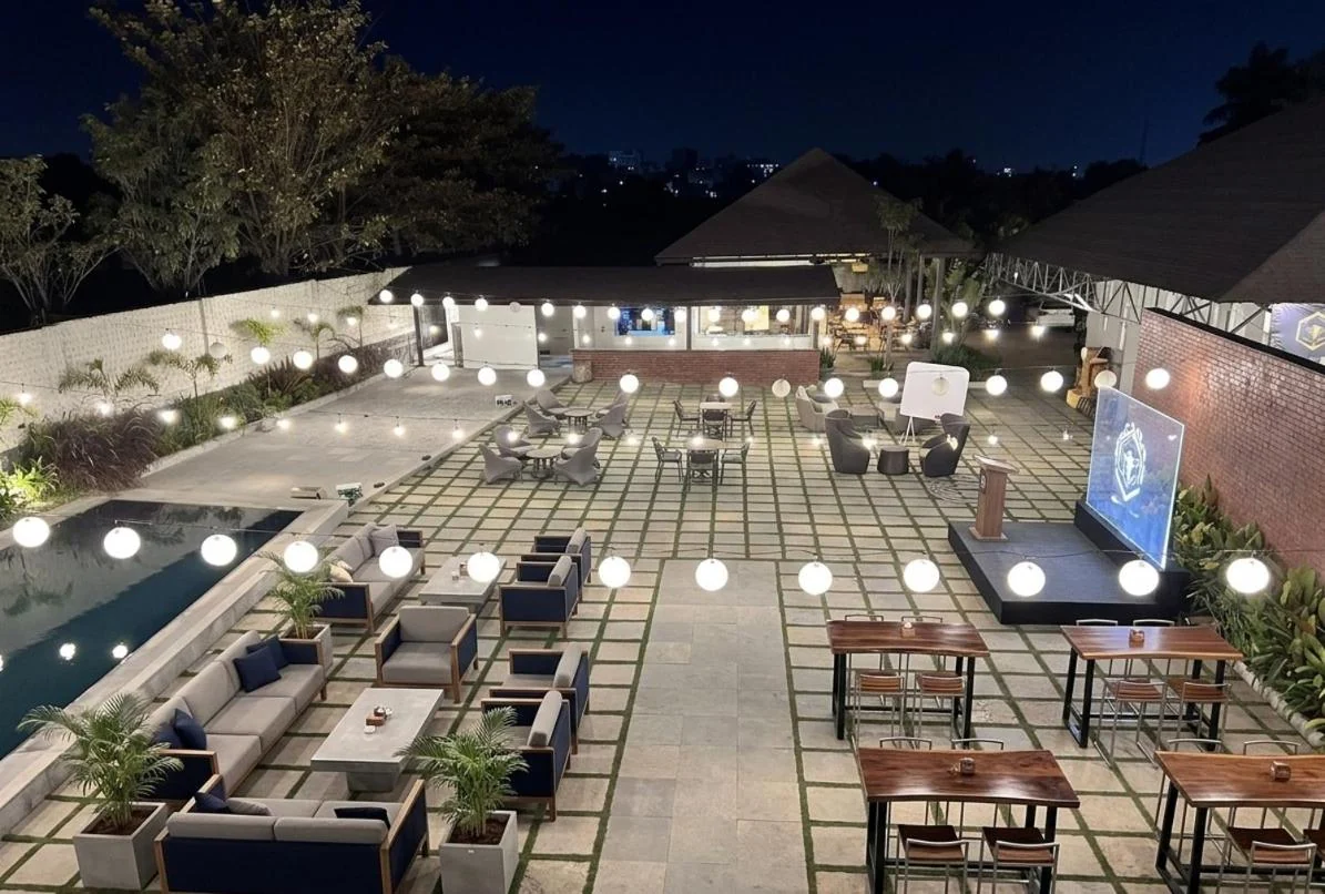 An elevated night view of Aavya Poolside Court with lounge seating, dining tables and lanterns