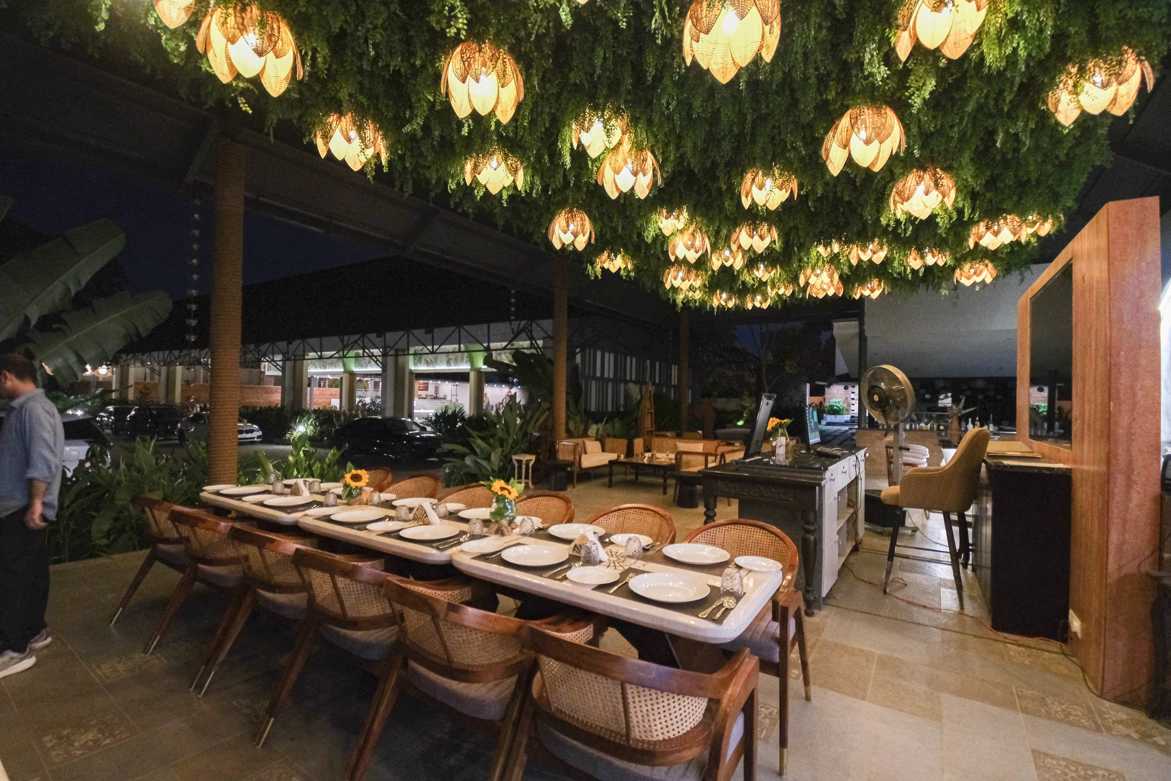 Samsara restaurant at night with a long dining table beneath leafy greenery and glowing woven lamps